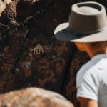 a man wearing a hat standing next to a rock