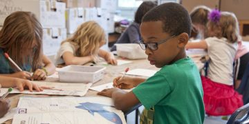 boy in green sweater writing on white paper