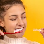 smiling girl in white sweater holding red and white toothbrush