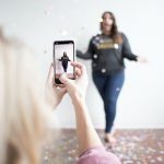 person holding white smartphone taking photo of woman wearing blue jeans