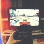 person holding Sony PS3 controller in front of flat screen monitor