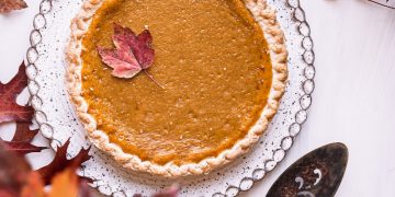 a pie sitting on top of a white table next to leaves