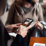 woman in brown coat holding black smartphone