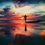 silhouette of person standing on rock surrounded by body of water