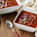 two bowls of chili and a spoon on a wooden table