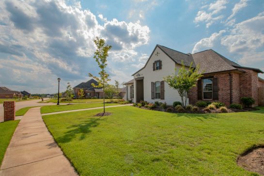 white and brown house near green grass field under white clouds and blue sky during daytime