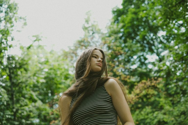 a woman standing in the woods with her hair blowing in the wind