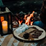 a person sitting in front of a campfire with a tray of marshmallow