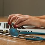 person sitting while using laptop computer and green stethoscope near