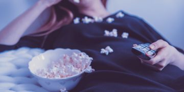 woman lying on bed while eating puff corn