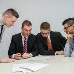 four men looking to the paper on table