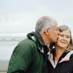 man kissing woman on check beside body of water