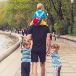 man in black t-shirt and brown shorts holding girl in blue and black jacket walking