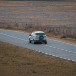 a car driving down a road in the middle of a field