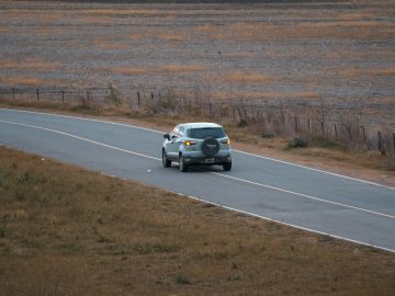 a car driving down a road in the middle of a field