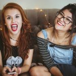 woman laughing beside woman smiling sitting on tufted sofa inside the room