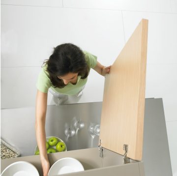 woman in green polo shirt and white pants standing in front of open cupboard