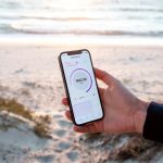 a person holding a cell phone with a beach in the background