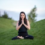 woman in black tank top and black pants sitting on green grass field during daytime