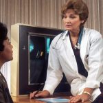 doctor sitting on desk talking to sitting woman