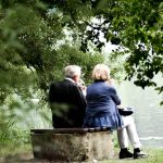 two people sitting on pavement facing on body of water