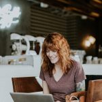 woman sitting on brown wooden chair while using silver laptop computer in room