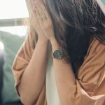 woman in brown shirt covering her face