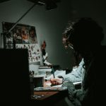 low light photography of woman in gray knit sweatshirt writing on desk