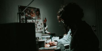 low light photography of woman in gray knit sweatshirt writing on desk