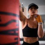 woman in black sports bra and black shorts holding orange bottle