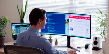 man in gray dress shirt sitting on chair in front of computer monitor