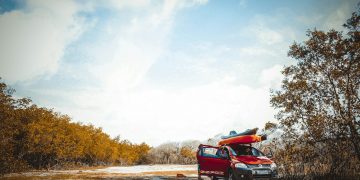 red vehicle on dirt road near trees at daytime